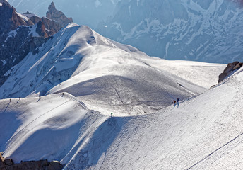 Fototapeta na wymiar Chamonix, south-east France, Auvergne-Rhône-Alpes. Climbers heading for Mont Blanc. Descending from Aiguille du Midi cable car station towards sunny snow planes and glaciers on border of France