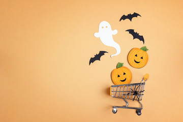 Shopping trolley with decorative pumpkins, ghost, bat and copy space on orange backdrop.  Halloween...