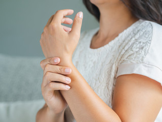 Closeup young woman sitting on sofa holds her wrist. hand injury, feeling pain. Health care and medical concept.