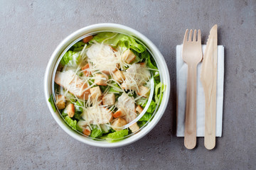Caesar salad in take away bowl on gray stone background, from above