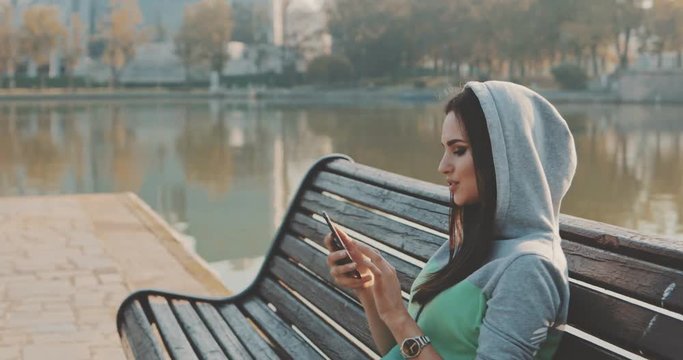 Brunette hipster woman wearing in hoodie selfie in park . Caucasian girl having fun with mobile phone , texting sending and reading messages , making photos . 4K video shooting by handheld gimbal