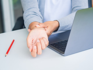 Closeup woman holding her wrist pain from using computer long time. Office syndrome concept.