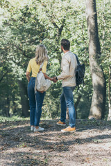 rear view of couple with backpacks holding hands while standing in park