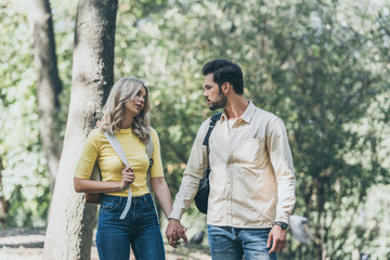 portrait of young couple with backpacks holding hands in park