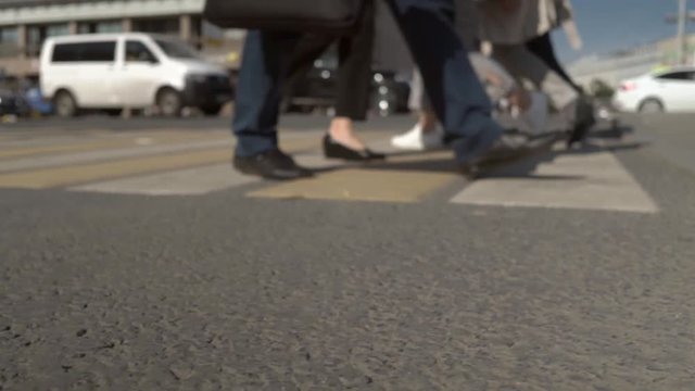 People's feet and legs are slowly walking along the pedestrian crossing. 
