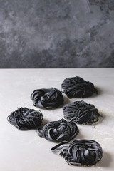 Variety of italian homemade raw uncooked cuttlefish ink black pasta spaghetti and tagliatelle with semolina flour on white marble table. Copy space.