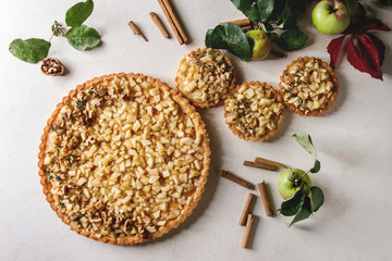 Homemade sweet apple shortbread tart and tartlets with cinnamon sticks, walnuts, apples branches...