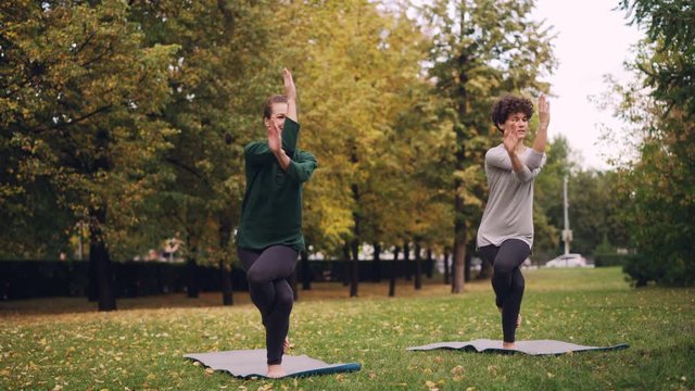 Slender girl yoga student is learning Eagle pose under guidance of teacher during individual practice with instructor in park. Beautiful autumn nature is in background.