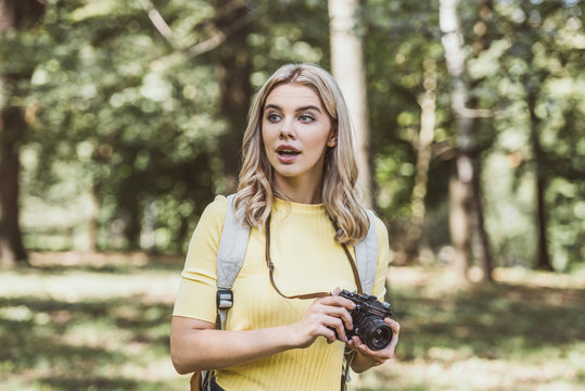 portrait of young emotional tourist with photo camera looking away in park