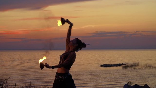 Woman near the river is dancing with fire bowls