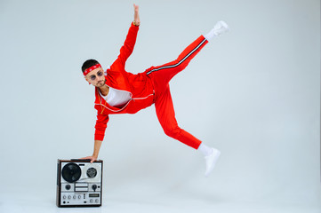 cheerful fashionable man wearing a red sports suit dancing jumps with a retro tape recorder....