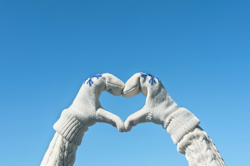 Female hands in the winter knitted  mittens in the shape of a heart on the clear blue sky background. Concept