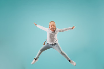 Fototapeta na wymiar Adorable small child at blue studio. The girl is jumping and smiling. Young emotional surprised teen girl. Human emotions, facial expression concept.