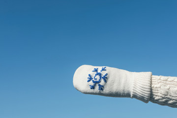 Female hands in the winter knitted mittens on the clear blue sky background. Concept