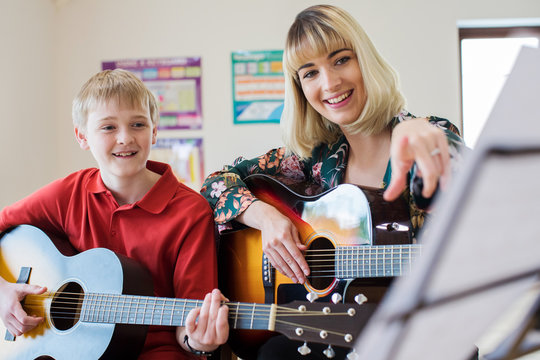 Teacher Helping Male Student To Play Guitar In Music Lesson