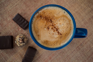 blue mug with coffee with milk and cinnamon on sack texture with some chocolate 