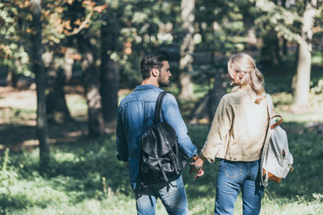 back view of young couple with backpacks walking in autumn park