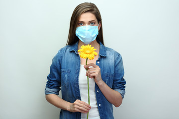 Young woman wearing medical mask holding yellow flower.