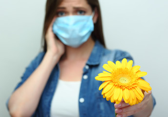 Young woman wearing medical mask holding yellow flower.