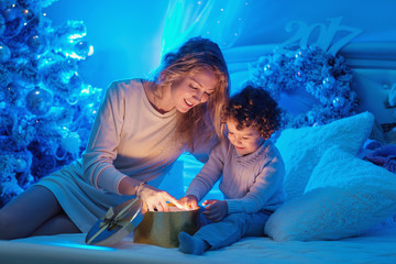 Young mother and her son are opening a Christmas gift box of shining light and magic. Happy family. Nativity night. Xmas holidays.