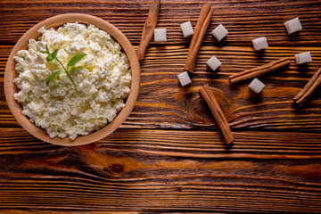 homemade cottage cheese in a wooden bowl, mint and sugar cubes, cinnamon lie on a wooden table