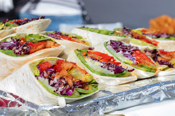 Wraps with meat and vegetable, cabbage, red pepper, tomato and lettuce. Metal tray with wraps, displayed offer for visitors of the Asian street food market.