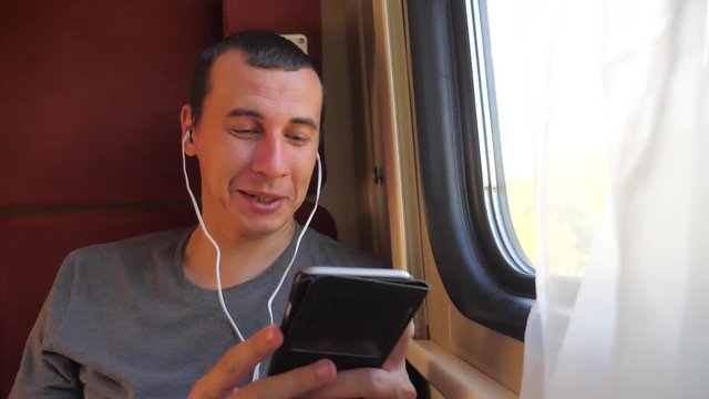 man listening to the music on the train rail car coupe compartment travel. slow motion video. man with a smartphone at the window of a train in a car travel internet lifestyle social media web. man