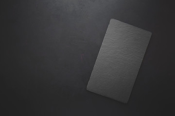Top view on rectangle black slate plate on rustic dark background. Copy space. Toned