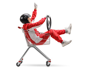 Mature man in a racing suit inside a shopping cart holding his hand up