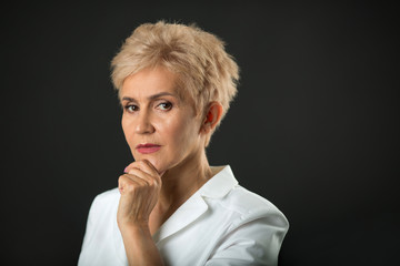 stylish woman in age with a short hairdo in a white jacket on a black background with a sad expression on her face