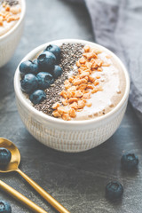 Banana dessert with chia seeds, fresh blueberry and nuts over a grey table.
