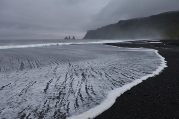 Expiring surf on the black beach near Vik i Myrdal, behind the Reynisdrangar rock needles, Myrdalur, Iceland, Europe