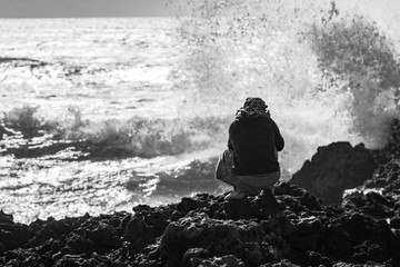 Photographing man on a rock in the background of a raging ocean. Black and white photography. The coast of the Atlantic Ocean. The beach is near Agadir. Africa Morocco
