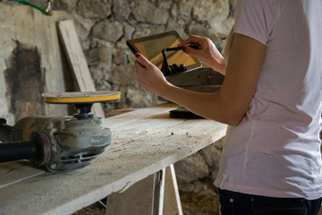 Crop view of female young adult with portable information device in hand makes a project  in a carpentry workshop
