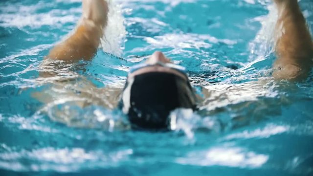 Disabled man swims on the back in a swimming pool towards the camera. Close up shot. Slow motion