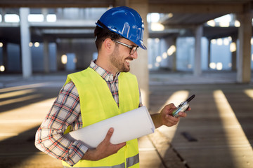Male architect with blueprints using walkie-talkie