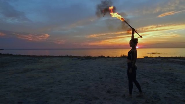 Beautiful woman is holding fire stick abowe her head at the beach