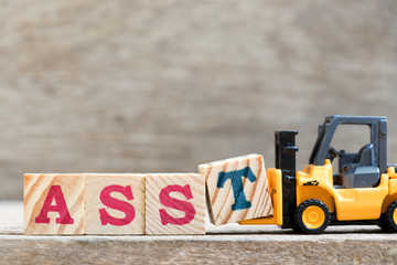 Toy forklift hold letter block T in word asst (abbreviation of assistant) on wood background