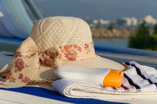 Close up of summer hat, towel and sun protection cream on a deck chair