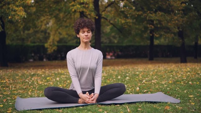 Pretty brunette is stretching legs in Cobbler's pose sitting on yoga mat then bending forward relaxing back and closing her eyes. Relaxation and yoga concept.