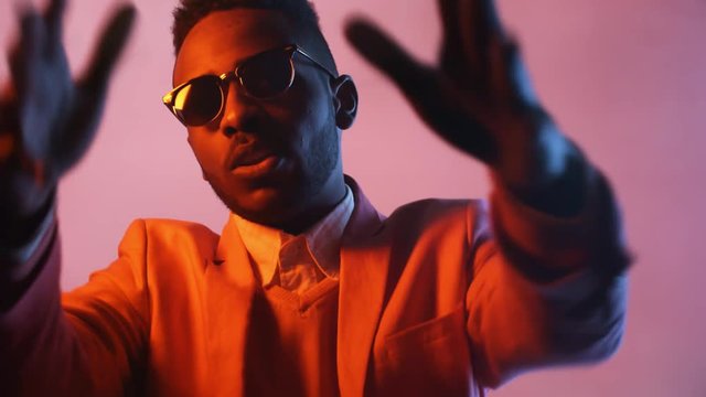 Portrait shot with use of color gel: confident black man in sunglasses rapping isolated on bright pink background in studio
