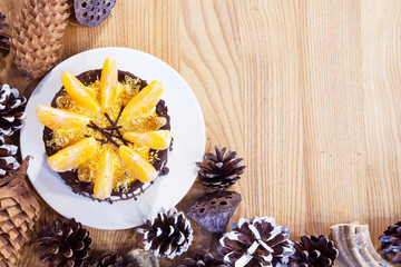 Торт с дольками мандаринов в окружении еловых шишек. 