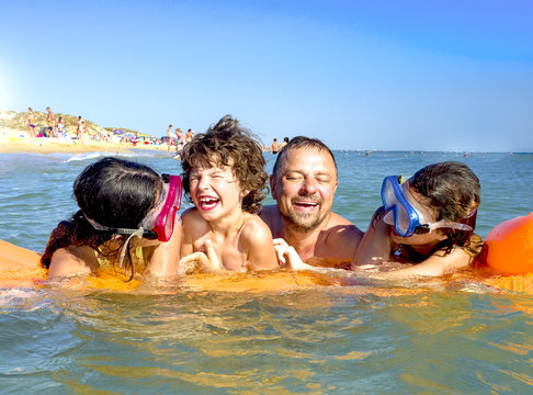 Happy father and three children have fun swimming in the sea on a vacation on the beach