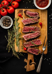 Slices of beef steak on meat fork on wooden cutting board.