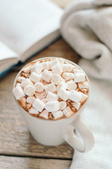Hot cocoa with marshmallow and spices on wooden table with a gray knitted plaid. Cozy breakfast, autumn weekend.