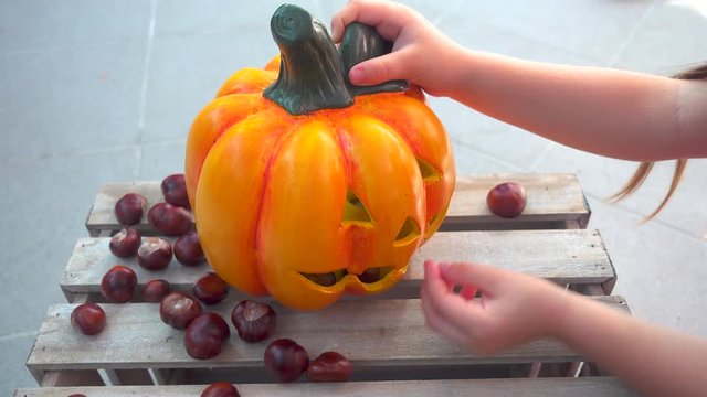 Little girl playing feeding chestnuts to halloween pumpkin, child play, holiday decoration, unrecognizable