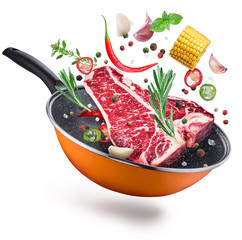 Flying T-bone steak and spices over a frying pan. File contains clipping path.