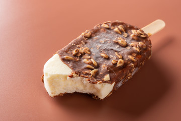 side view chocolate outer ice cream with peanuts on a brown background with some bites