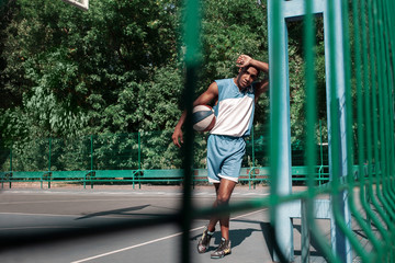 Picture of young confused african basketball player practicing outdoor. Fit afro man resting after movement. athletic and sport lifestyle concept