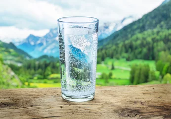 Zelfklevend Fotobehang Glas water op de steen. Wazig sneeuw bergen toppen en groene bossen op de achtergrond. © volff